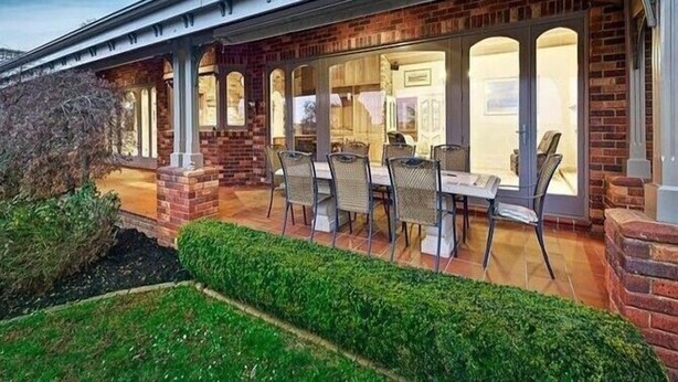 A covered patio with outdoor seating, brick walls, and a glass door leading to an interior space. - Oak Hill Grand Country Escape with Sunset Views (Chirnside Park)