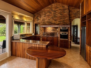 A kitchen with a brick wall, wooden cabinets, a built-in oven, and a large island with a round table.