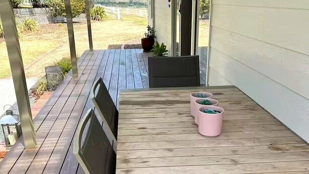 Eine Holzterrasse mit Tisch und Stühlen, einem Blumentopf und Blick ins Freie.