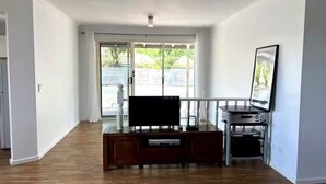 Ein Wohnzimmer mit Flachbildfernseher, einer Holzunterhaltungsecke und einem großen Fenster mit Blick auf einen Garten.