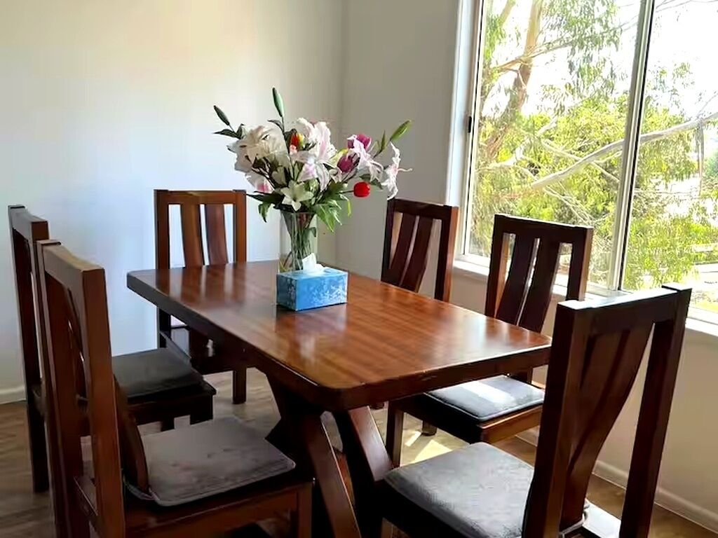 A dining table with six chairs, a vase with flowers, and a blue box on the table.