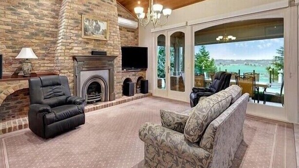 A living room with a stone fireplace, leather chairs, a sofa, and a large window with a view. - Oak Hill Estate - Main House plus Cottage (Chirnside Park)