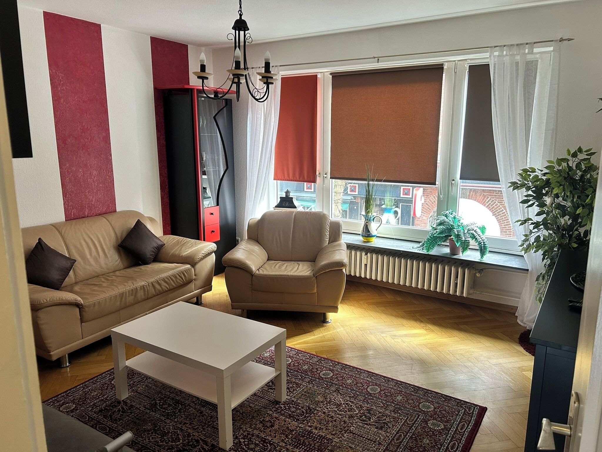 Un salon comprenant un canapé, un fauteuil, une table basse, un radiateur et une fenêtre avec des rideaux.