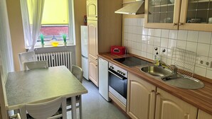 Una cocina compacta con una mesa de comedor, horno empotrado, lavamanos y ventana con cortinas.