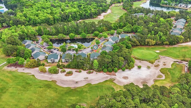 Vista aérea de un campo de golf con club house, rodeado de vegetación densa y un lago.