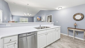 Una cocina con armarios blancos, lavavajillas de acero inoxidable, un lavabo y una lámpara colgante.