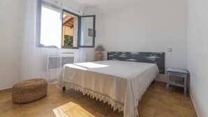 Une chambre à coucher avec un lit, une fenêtre, une petite table et un tabouret en osier.
