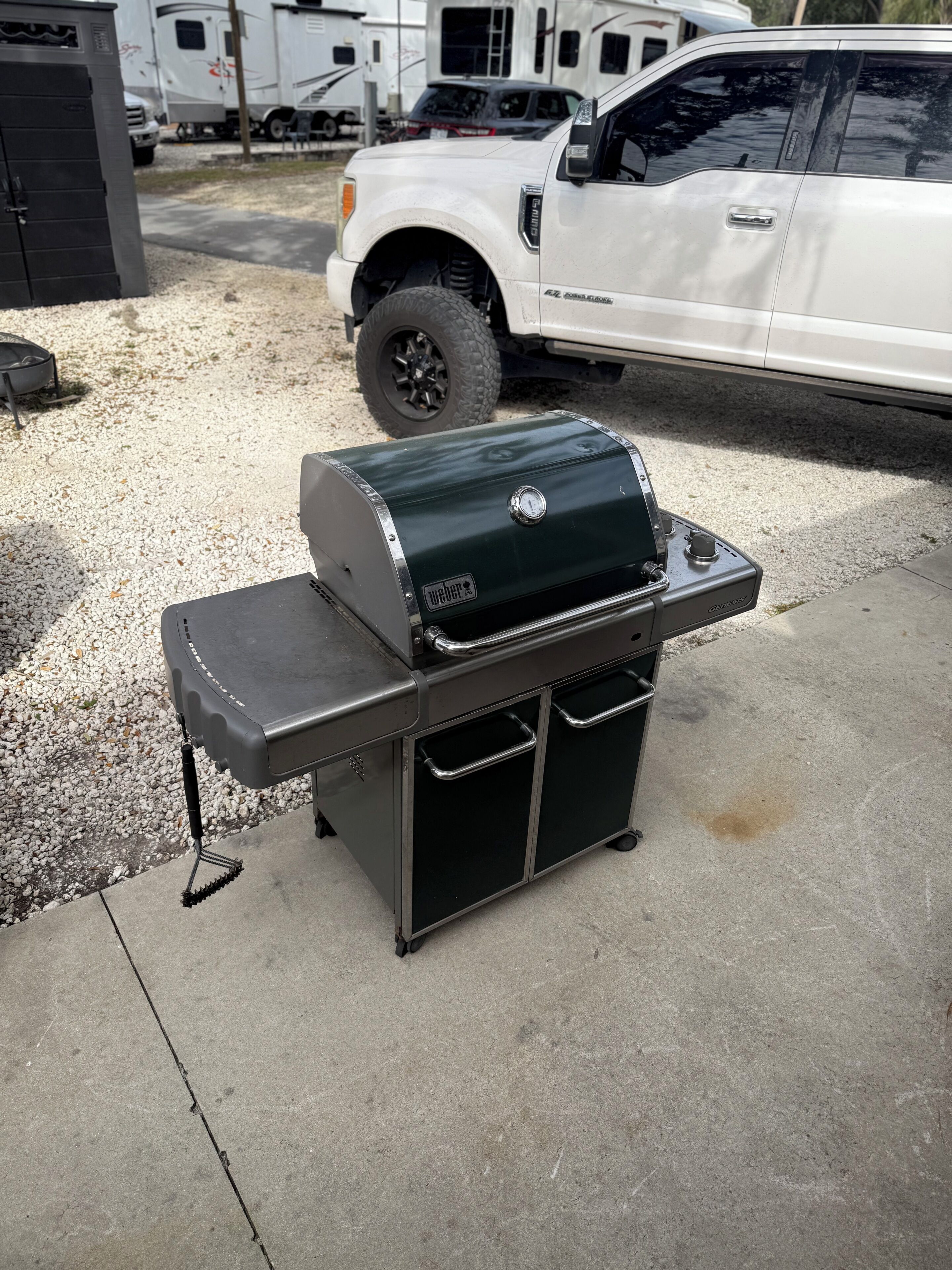 A portable grill with a side table, wheels, and a digital thermometer.