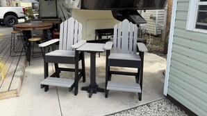 Un patio al aire libre con dos sillas Adirondack, una mesa redonda y una parrilla.