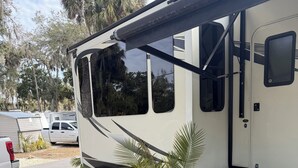 Un vehículo recreativo con un porche cubierto, mobiliario exterior y una rampa que lleva a la entrada.