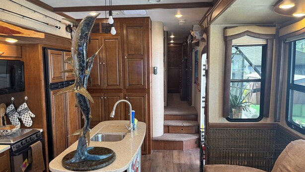 Cocina con muebles de madera, una isla central con pileta, microondas y horno. Una escalera lleva a un balcón con vistas.