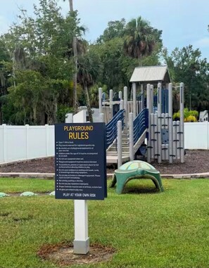 A playground with a sign listing rules and a play structure.