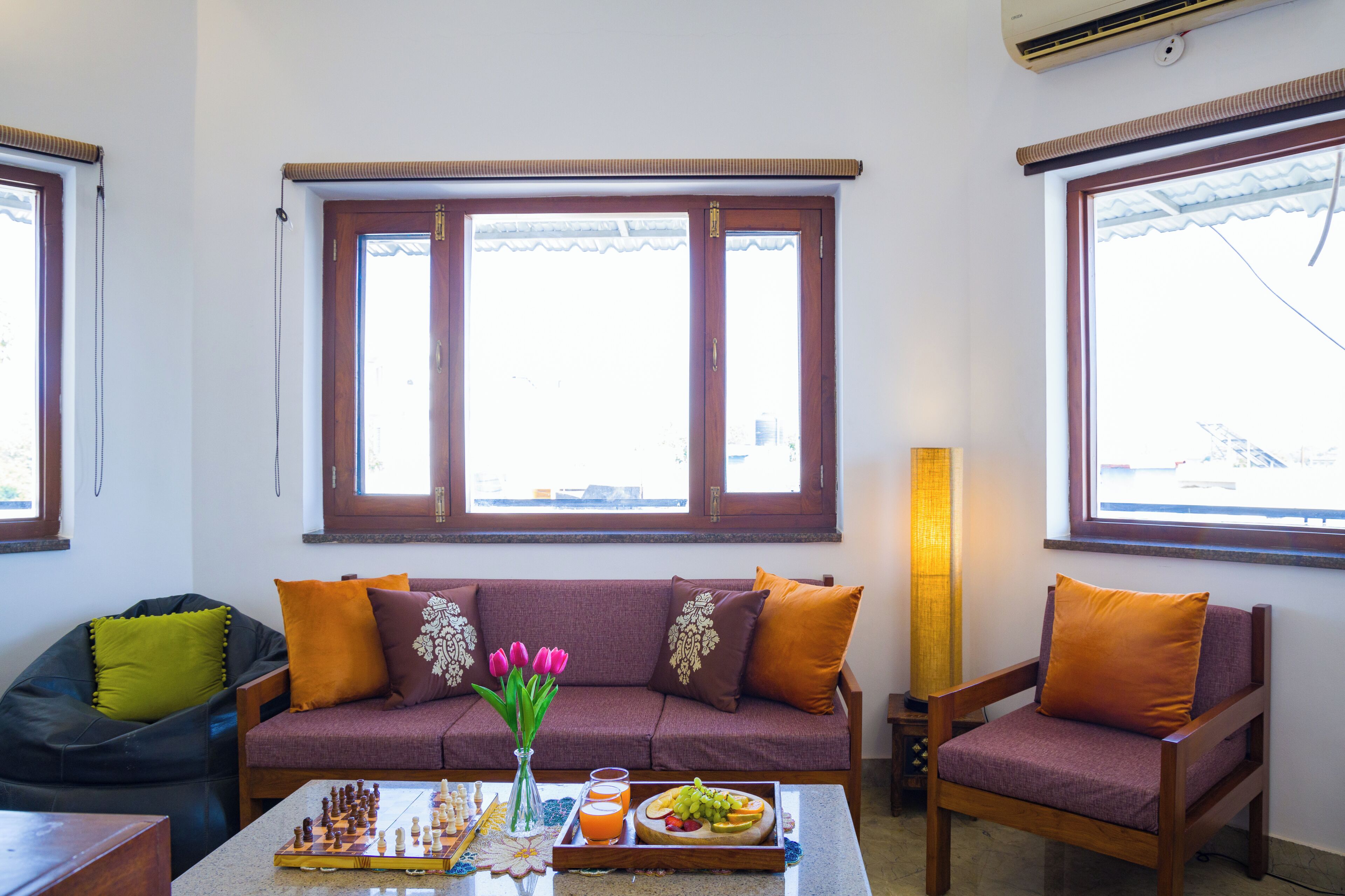 A living room with a sofa, a chair, a chessboard, and a tray with fruit and drinks.
