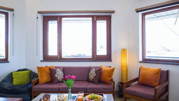 A living room with a sofa, a chair, a chessboard, and a tray with fruit and drinks.