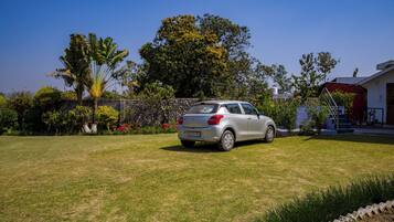 A car parked in a grassy area with a stone wall, trees, and a building in the background.