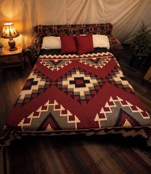A bed with a patterned blanket, a bedside lamp, and a small table with a plant. - Soaring Dreams Tepee | King Bed | Resort Access (Sevierville)