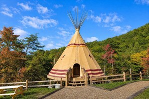 Un tipi traditionnel, avec une échelle menant à l’entrée, entouré d’une clôture en bois et de tables de pique-nique.