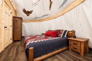 Une pièce chaleureuse avec un lit, des tables de chevet en bois et un plafond en forme de tente orné d’illustrations d’oiseaux.
