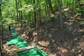 A miniature golf course set in a wooded area with multiple green putting lanes. - Soaring Dreams Tepee | King Bed | Resort Access (Sevierville)