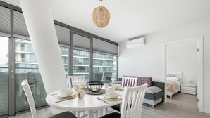 Una stanza moderna e luminosa, con un tavolo da pranzo apparecchiato per quattro persone, un divano, un comodino e un'ampia finestra con persiane.