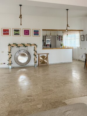 Un espacio habitable amplio con cocina, una pared decorativa con obras enmarcadas y un lámpara colgante.