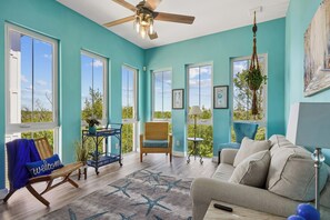 A room with large windows, a ceiling fan, a wicker chair, a sofa, and a hanging plant. - Mangrove Walk-30+ Day Rental in Harbour Isle in Perico (Bradenton)