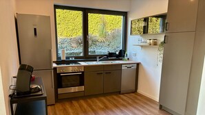 A modern kitchen with a built-in oven, a dishwasher, and a coffee machine on a stand. - RaumWerk Apartment • family-friendly - Terrace (Wülfershausen an der Saale)