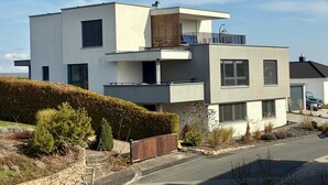 A modern multi-story residential building with a flat roof, large windows, and a balcony. - RaumWerk Apartment • family-friendly - Terrace (Wülfershausen an der Saale)