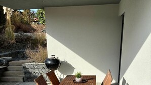 A patio with a wooden table and chairs, a grill, and potted plants. - RaumWerk Apartment • family-friendly - Terrace (Wülfershausen an der Saale)