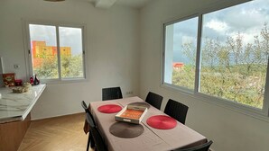 A dining area with a table set for four, chairs, a hanging light fixture, and large windows with a view of buildings and trees.
