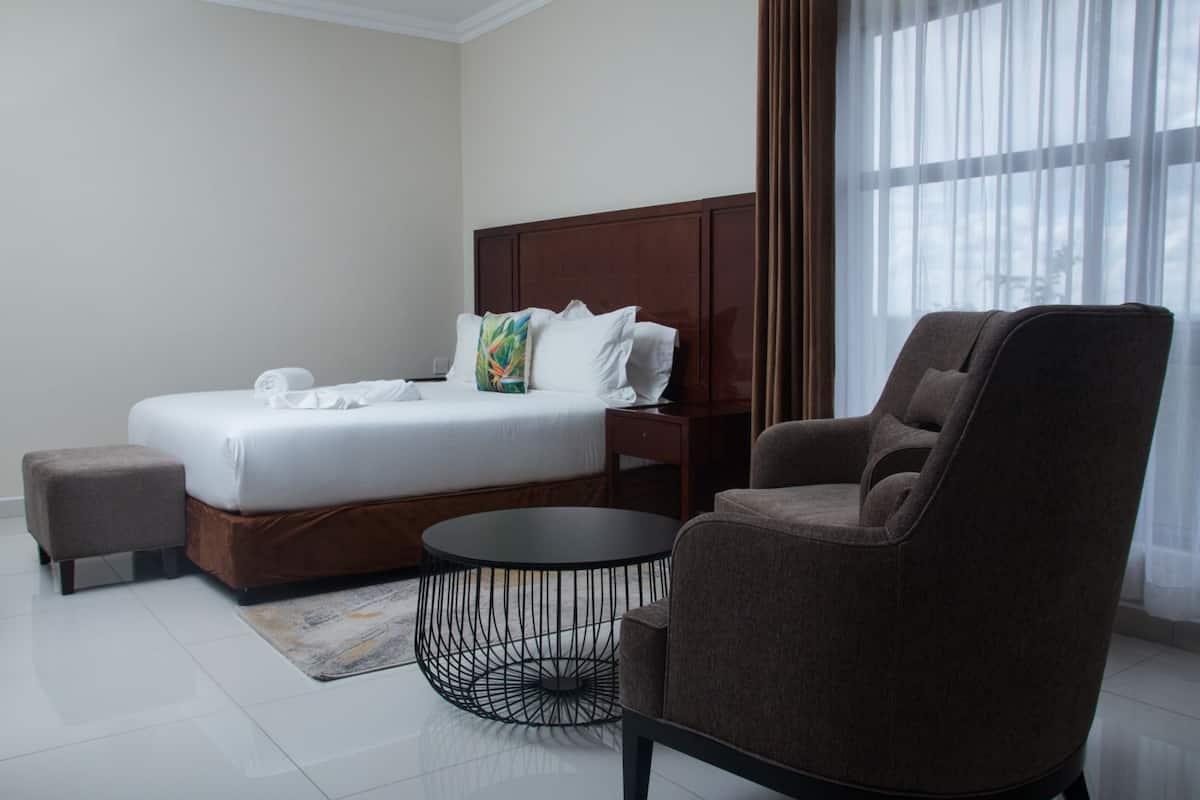 A hotel room with a bed, a round coffee table, a brown armchair, and a nightstand.