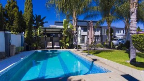 Une piscine avec des chaises longues, des palmiers et un bâtiment en arrière-plan.