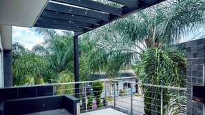 Un balcon avec un canapé noir, une rambarde en métal et une végétation luxuriante en arrière-plan.