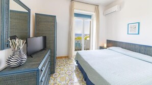 A hotel room with a bed, a television, a dresser, a mirror, a window with curtains, and an air conditioning unit.
