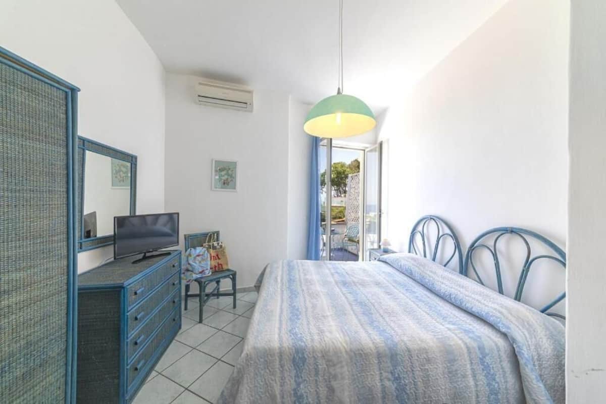Ein Schlafzimmer mit Bett, Kommode, Fernseher und einem Fenster mit Blick.