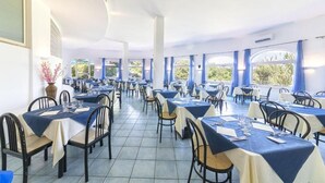 A restaurant with tables set for dining, large windows, and a tiled floor.
