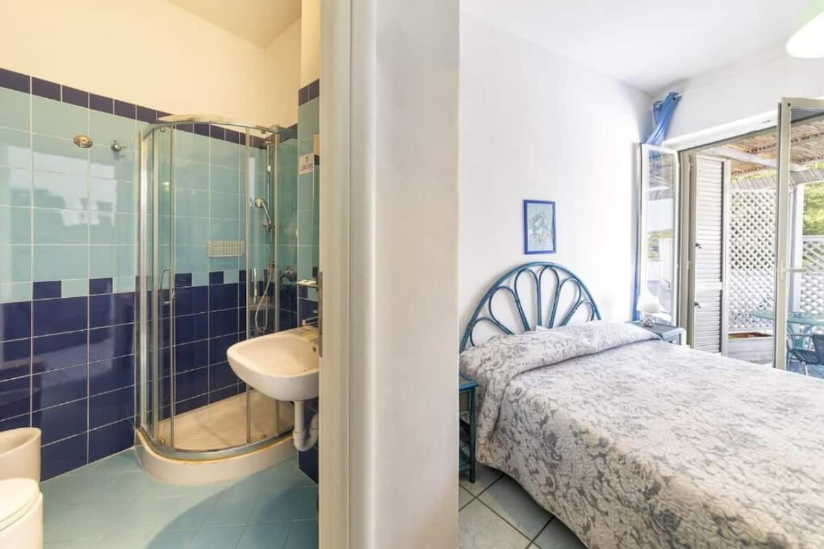 Ein Badezimmer mit Glasdusche, Waschbecken und einem Bett mit gemustertem Überwurf.