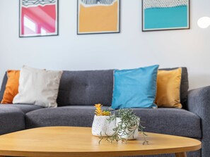 A grey sofa with multiple cushions, a wooden coffee table, and two potted plants. - Casa Sardinha - in the heart of Portimão (Portimão)
