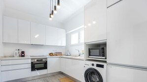 A modern kitchen with white cabinetry, a built-in oven, a microwave, and a front-loading washing machine. - Casa Sardinha - in the heart of Portimão (Portimão)
