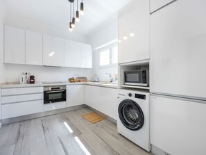 Une cuisine moderne avec des meubles blancs, un four encastré, un four à micro-ondes et un lave-linge à chargement frontal.