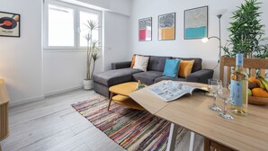 A modern living room with a sofa, coffee table, and a dining table with glasses and a bottle. - Casa Sardinha - in the heart of Portimão (Portimão)