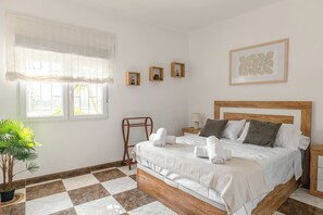 Un dormitorio con cama, ventana con cortina translúcida, una planta pequeña y un cuadro en la pared.