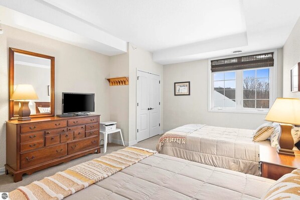 A bedroom with a bed, a dresser, a television, a desk, and a window with a view. - Bird's Eye View at Hawk's Eye (Bellaire)