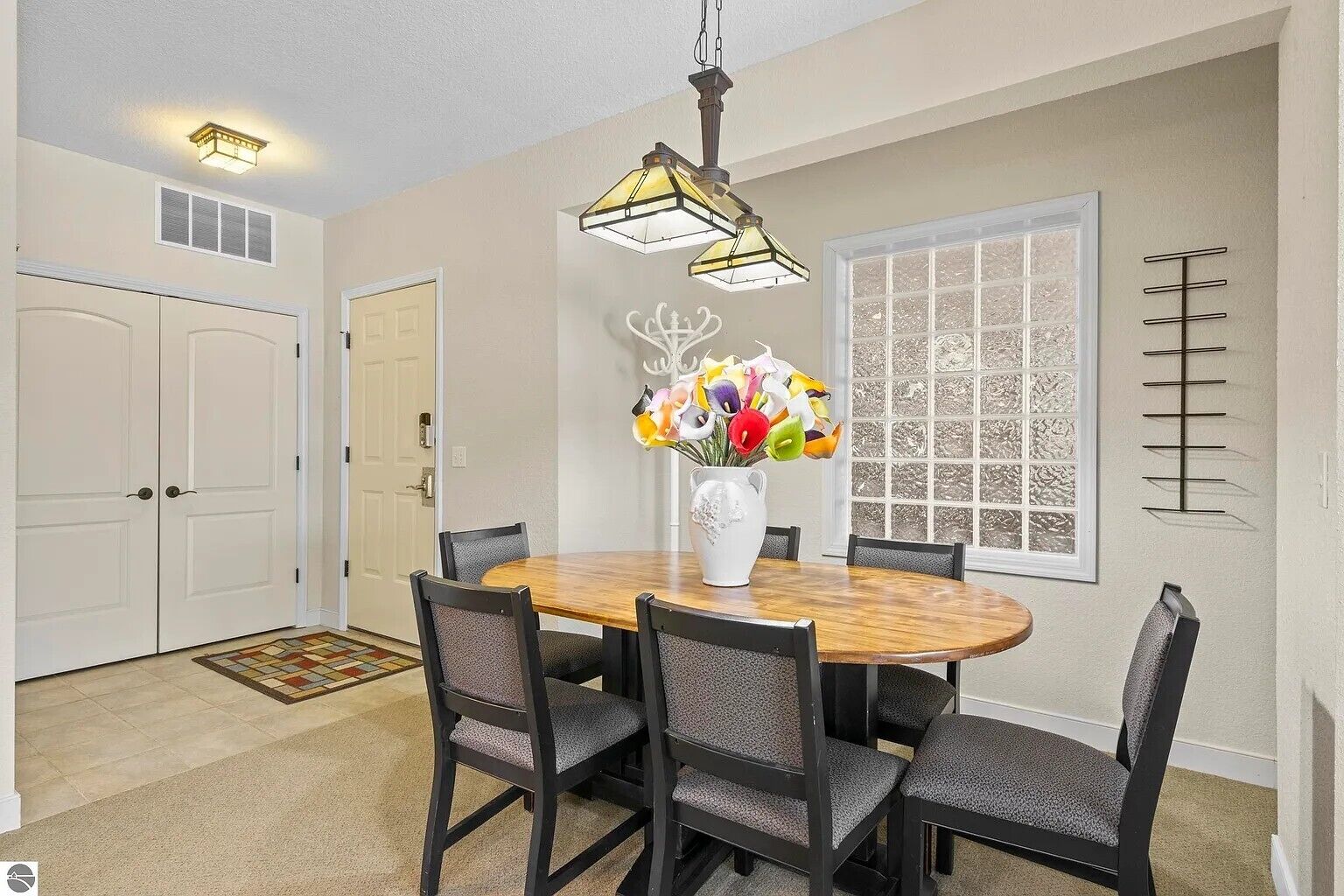 A dining room with a round table, six chairs, a vase of flowers, a window with a view, and a ceiling light fixture.