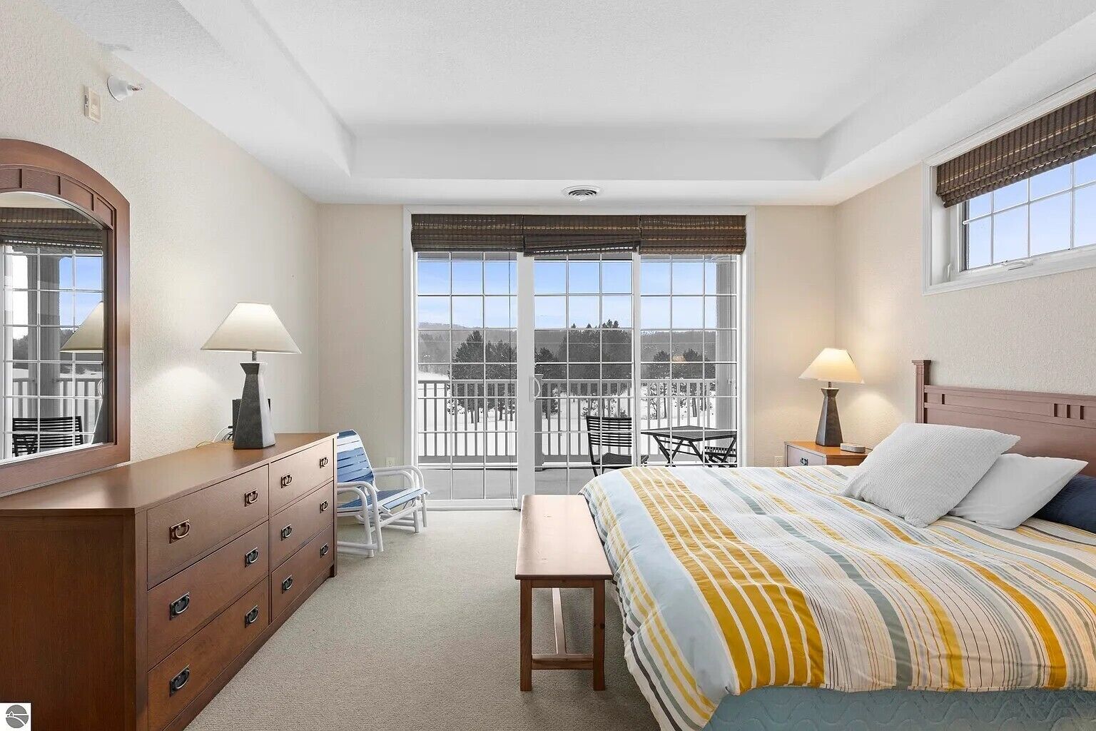 Ein Schlafzimmer mit Bett, Nachttischen, Kommode, Stuhl, Bank und einem großen Fenster mit Blick.