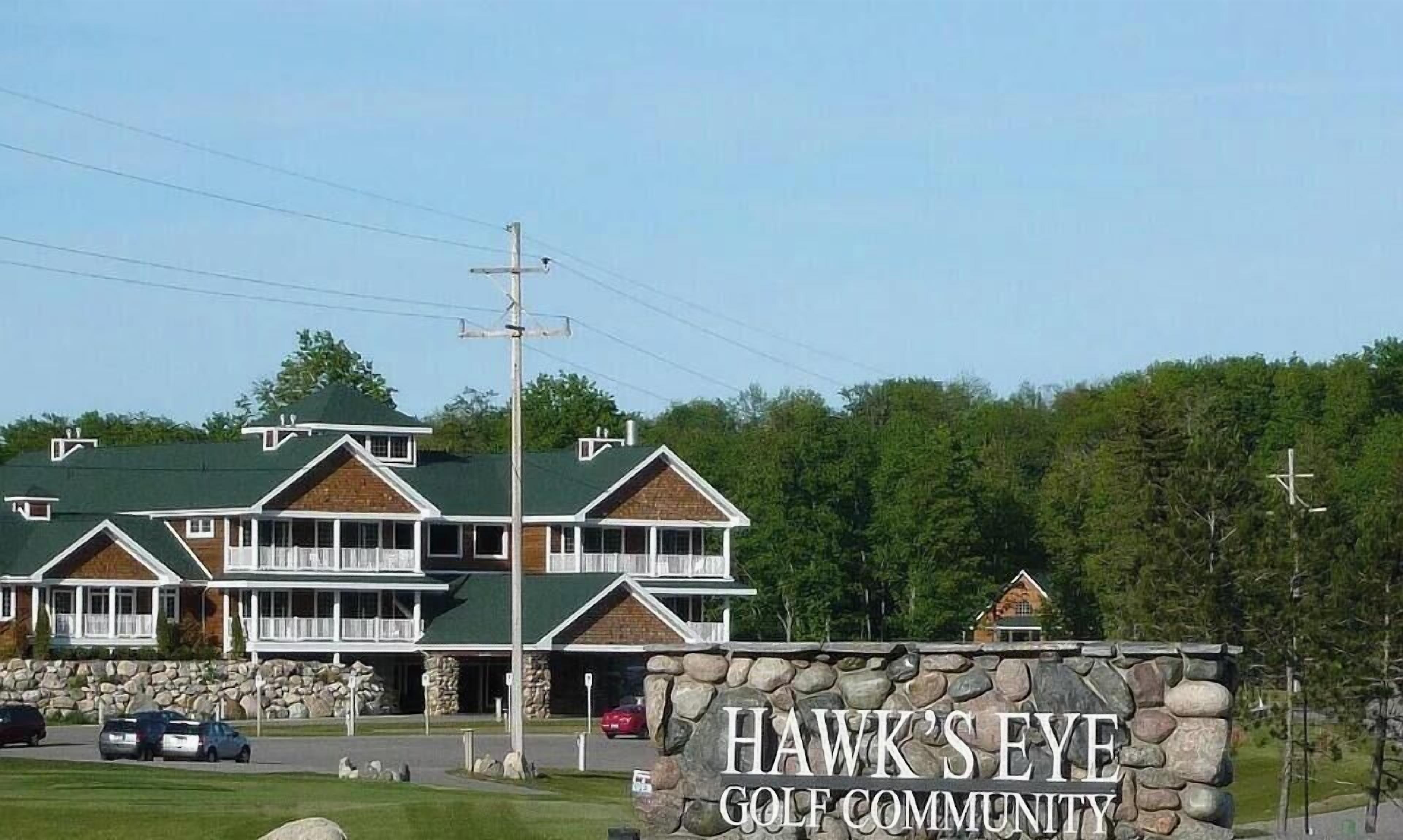 A two-story building with a stone facade and a green roof, labeled 'Hawk's Eye Golf Community.'