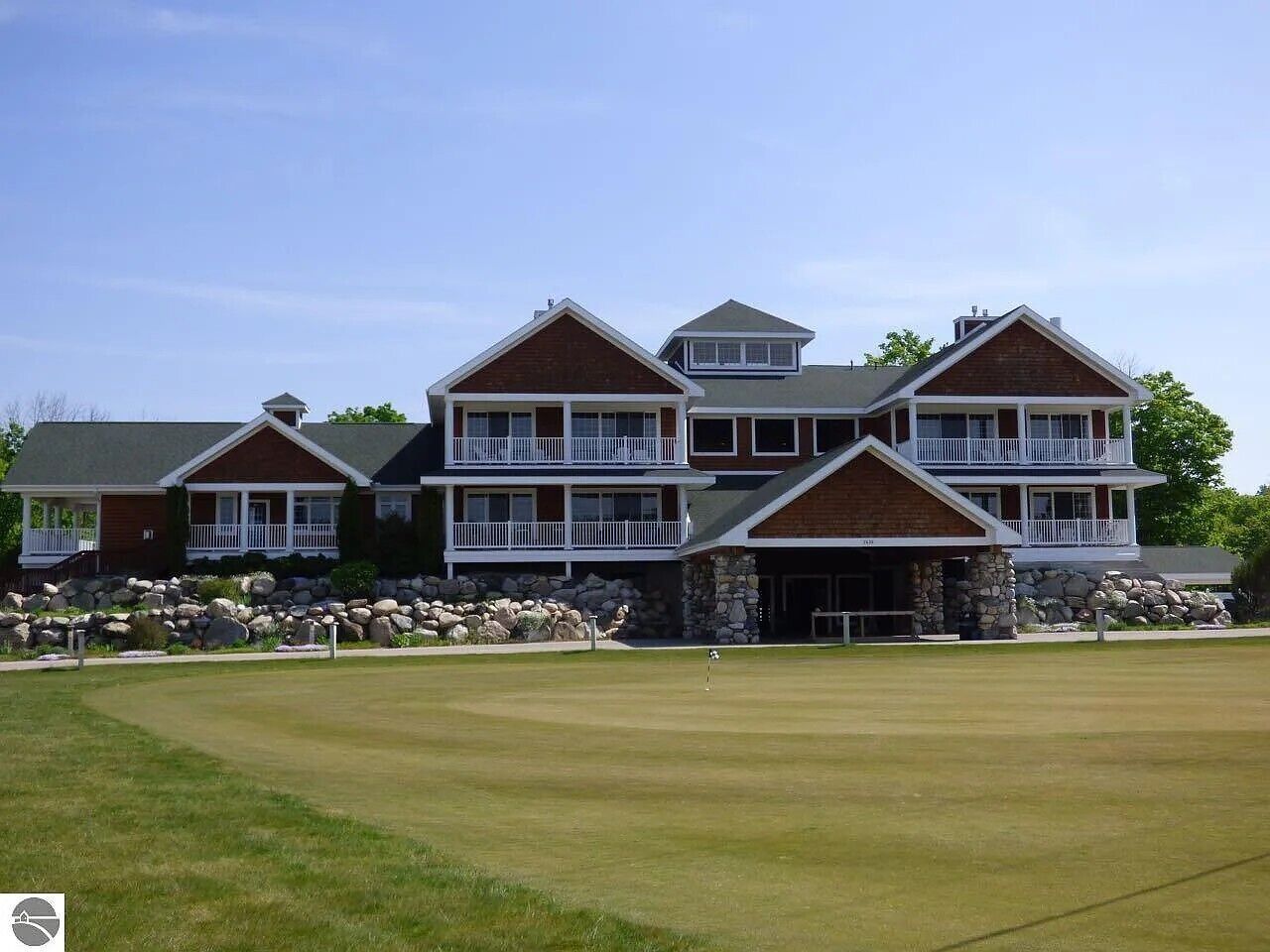 A large, multi-story building with a stone facade, a balcony, and a well-maintained lawn in front.