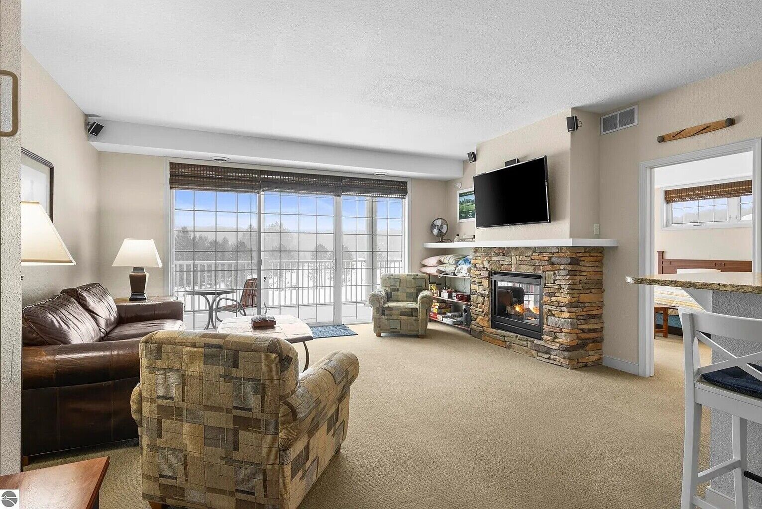 A living room with a stone fireplace, a television mounted on the wall, and a large window with a view.