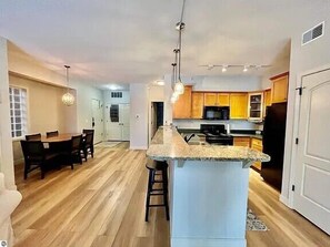 A spacious kitchen with a central island, wooden flooring, and a dining area with a table and chairs.