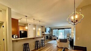 Una cocina moderna con una isla central, taburetes de bar y un comedor con mesa y sillas de madera.